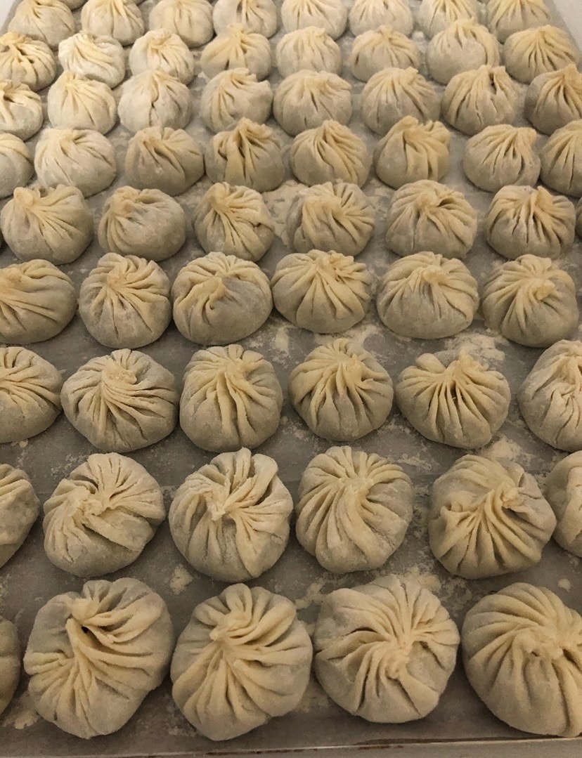 Rows of freshly folded dumplings on a floured tray ready to steam